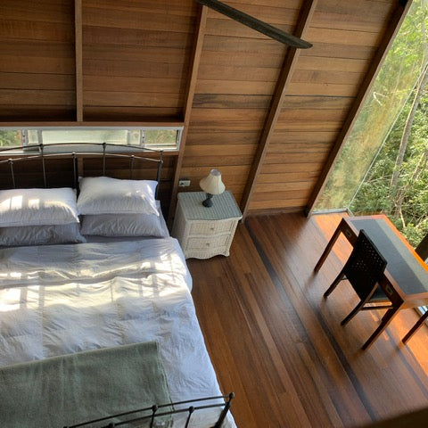 Bridge Cabin master bedroom.  Wood cabin interior with high ceiling and work desk in bedroom.  Large windows with sunlight pattern on comforter.  Wood floors and and walls. Steel beam frame. Best cottage in Trinidad. Where to stay in Trinidad